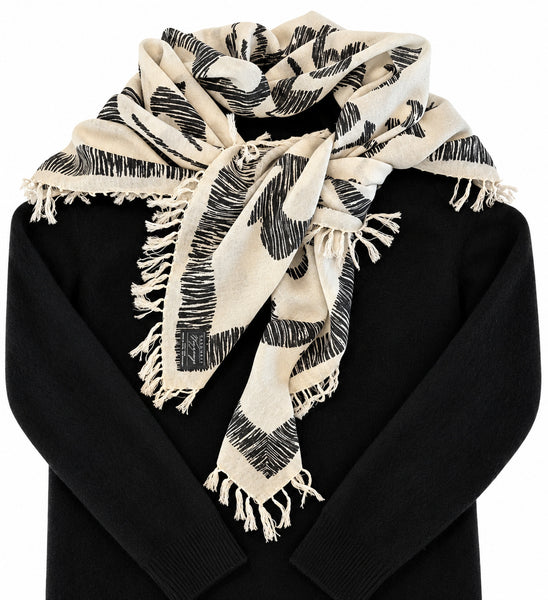 Black and ivory damask Merino wool scarf styled over a black sweater, showing its generous drape, graphic botanical pattern and hand-knotted fringe.